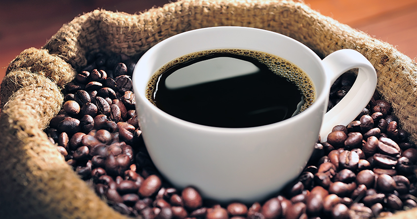 En hvit kopp med svart kaffe står oppi en pose med kaffebønner