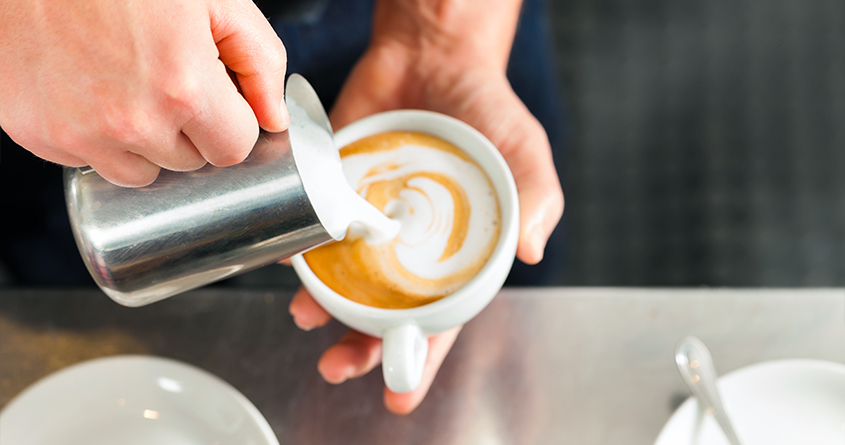 En barista heller steamet melk oppi en kopp med cappuccino