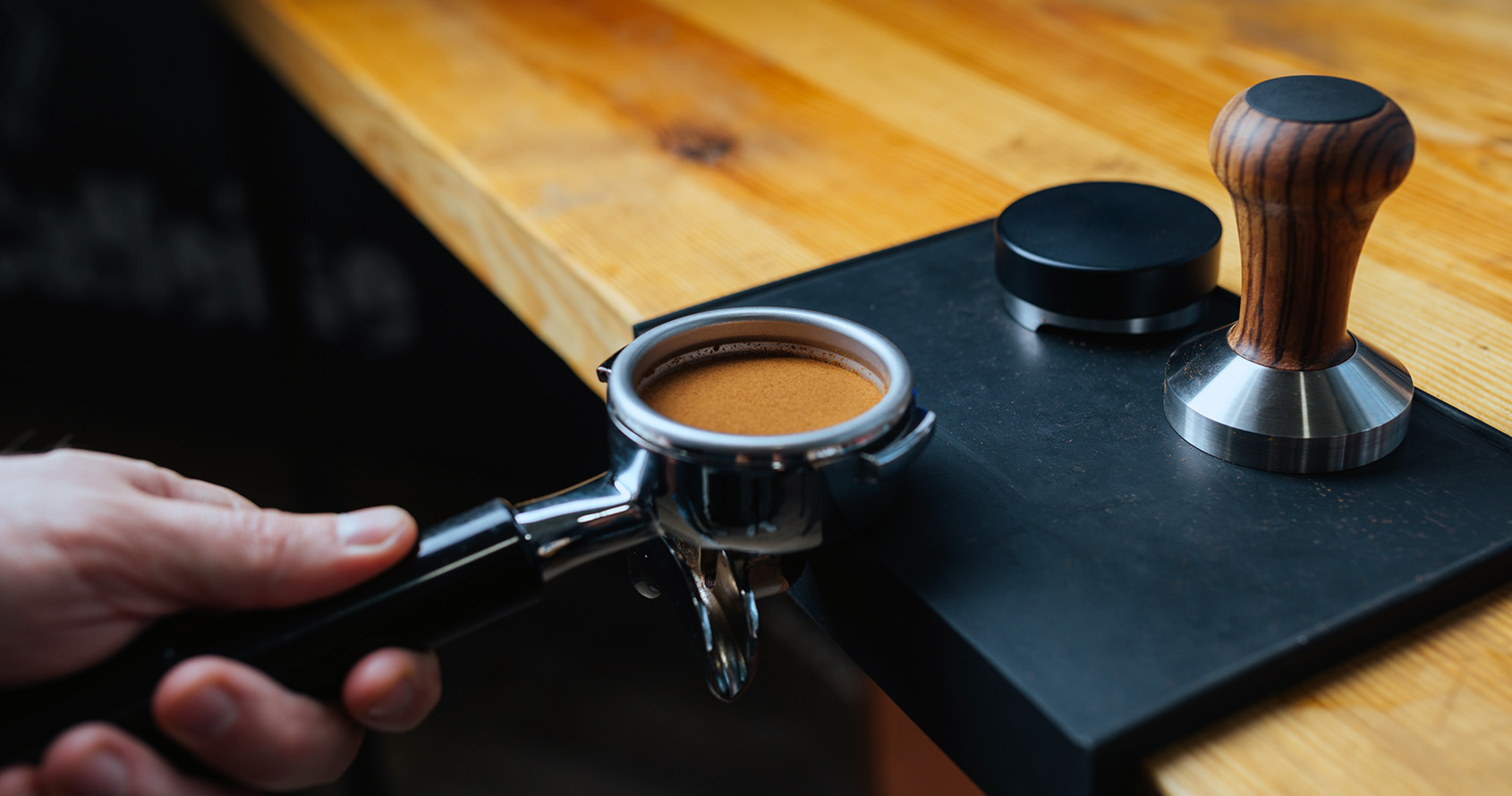 En person holder et portafilter med en tampet kaffepuck