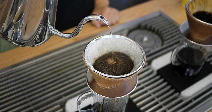Noen heller kokende vann fra en vannkoker over kaffe i en Steadfast Coffee Brewer