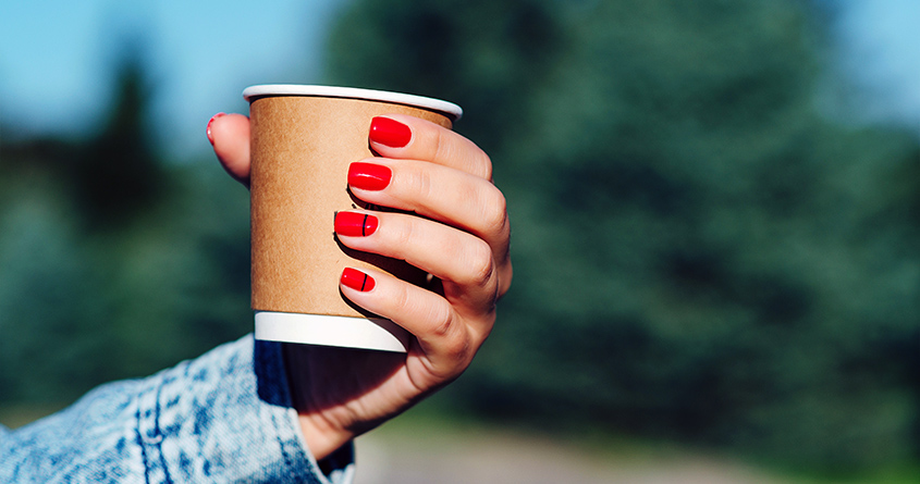 En kvinne med røde negler holder opp en engangskopp med kaffe