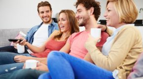 Fire unge mennesker smilende med kaffekopper i en sofa