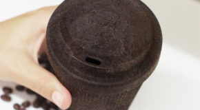 En hånd holder en brun kopp med lokk.