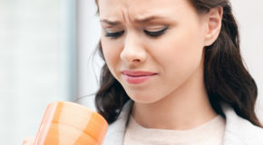 En kvinne lager en grimase når hun drikker kaffe med en dårlig smak.