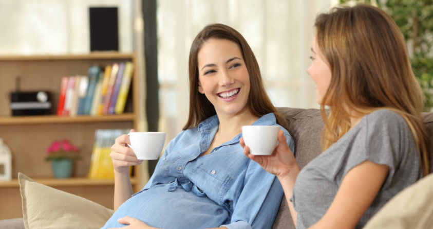 To kvinner drikker kaffe i en sofa. Den ene er gravid.