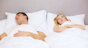 En mann ligger i en dobbeltseng og sover, mens kvinnen ved siden av ligger våken.