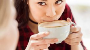 En kvinne drikker en kaffe med melkeskum