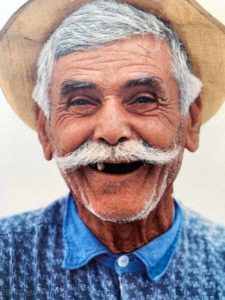 En smilende gresk mann med bart og hatt.