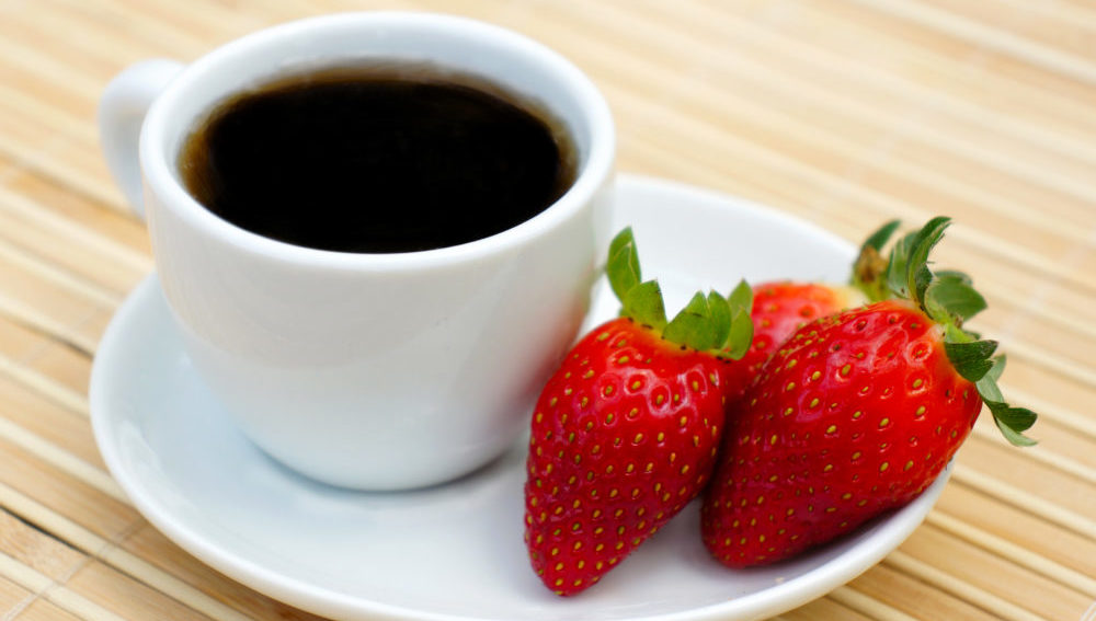 En kaffekopp og jordbær på en asjett.