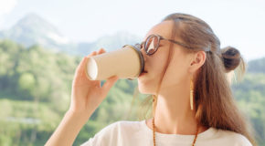 En kvinne med solbriller drikker kaffe. Solfylt landskap i bakgrunnen.