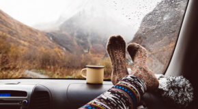 En kvinne har føttene sine på dashboardet i en bil ved siden av en kopp kaffe