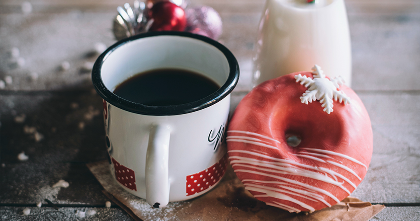 En julekopp med kaffe står på en skjærefjøl ved siden av en donut