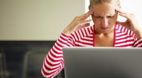 En kvinner sitter foran en laptop og tar seg til hodet.