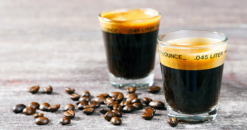 To shotteglass med espresso står på et bord sammen med en håndfull kaffebønner