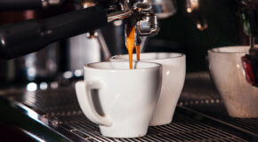 Nybrygget espresso renner ut av portafilteret og oppi to hvite kopper.