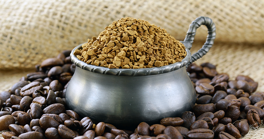 En liten potte med pulverkaffe står på et bord, omringet av kaffebønner