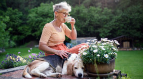 En eldre kvinne sitter i hagen sammen med hunden sin og drikker kaffe