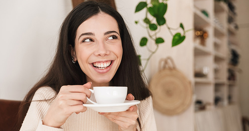 En kvinne drikker kaffe og ser glad ut.