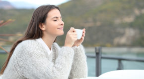 En ung kvinne lukter på kaffen sin og nyter den ute i naturen