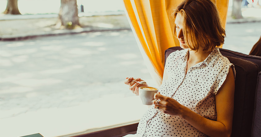 En gravid kvinne ser ned på en kaffekopp.