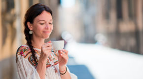 En kvinne ser ned på kaffekoppen hun holder mellom hendene.