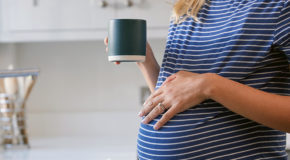 En gravid kvinne holder en hånd på magen og en kaffekopp i den andre hånden
