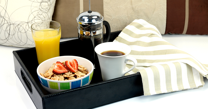 Frokost på senga med frokostblanding, appelsinjuice og kaffe i presskanne