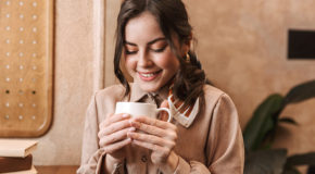 En kvinne smiler og ser ned på en kopp med kaffe, som kan motvirke depresjon.