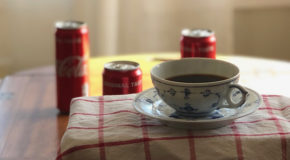 En kaffekopp med cola står på et bord sammen med colabokser.
