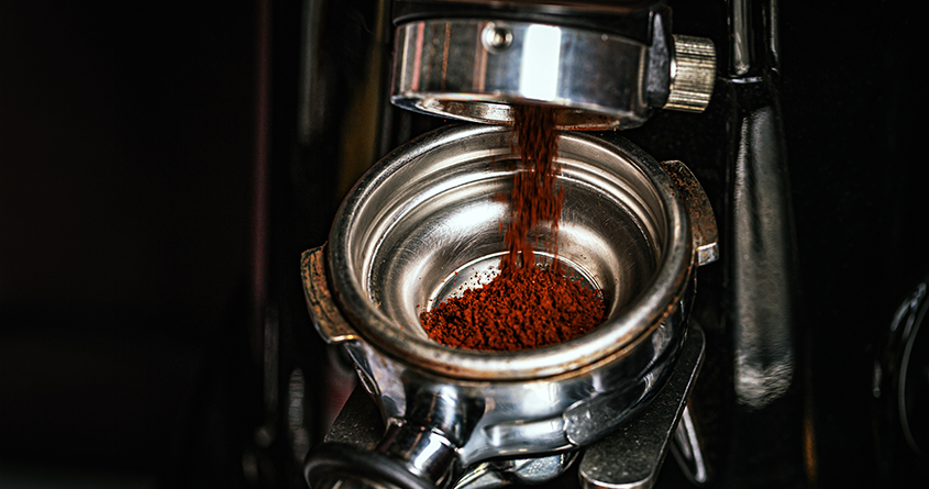 Nærbilde av kaffe som kvernes ned i en tamper til espresso.