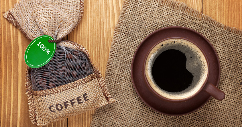 En kaffepose med kaffebønner ligger på bordet ved siden av en kaffekopp med traktet kaffe