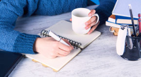 En person drikker kaffe mens de skriver i en notatbok - kanskje skriver de om kafferegler.