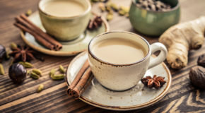 To kopper med chai latte står på et bord, sammen med drøssevis av forskjellige kryddere