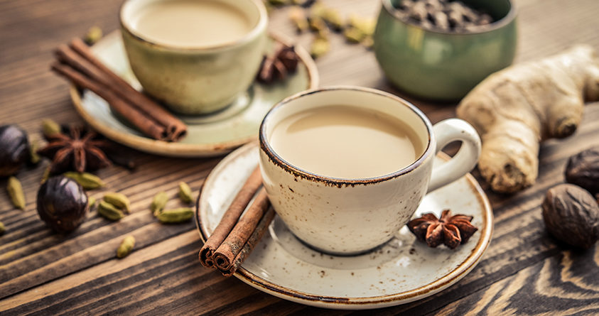 To kopper med chai latte står på et bord, sammen med drøssevis av forskjellige kryddere