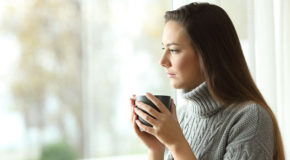 En kvinne ser ut av vinduet og drikker kaffe.