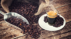 Et glass med espresso står på et bord sammen med kaffebønner.