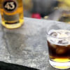 Et glass med isbiter og Carajillo 43 står på et bord med en flaske Licor 43 i bakgrunnen