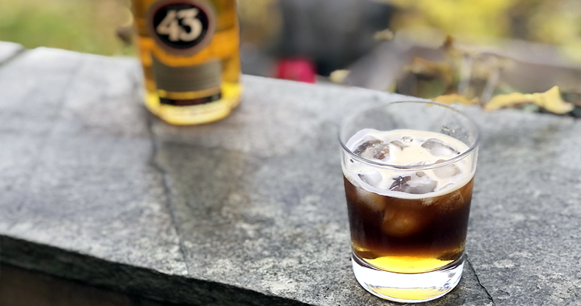 Et glass med isbiter og Carajillo 43 står på et bord med en flaske Licor 43 i bakgrunnen