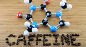 Et koffeinmolekyl ligger på et bord med teksten «caffeine» skrevet under i kaffebønner.
