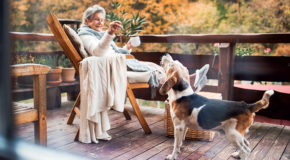 En eldre dame sitter og drikker kaffe og leker med hunden sin.