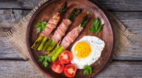 En tallerken med asparges, bacon, egg og tomat står på et bord.
