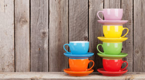 Seks kopper i forskjellige farger står på et bord.