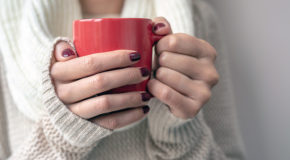 En ung kvinne holder rundt en rød kopp med kaffe.