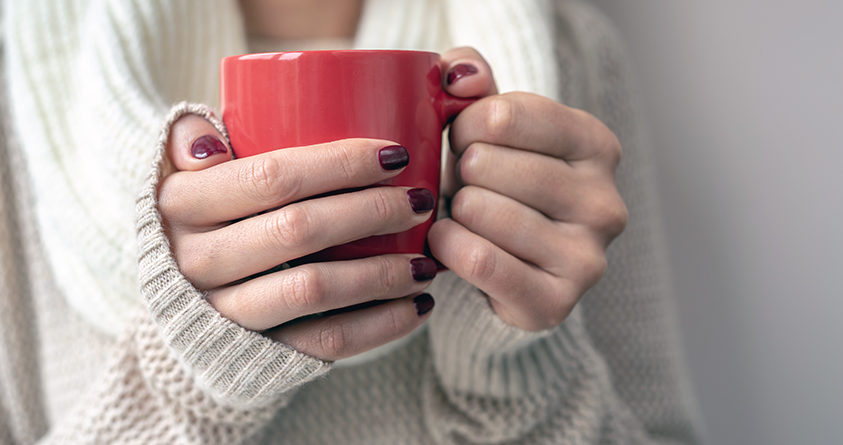 En ung kvinne holder rundt en rød kopp med kaffe.