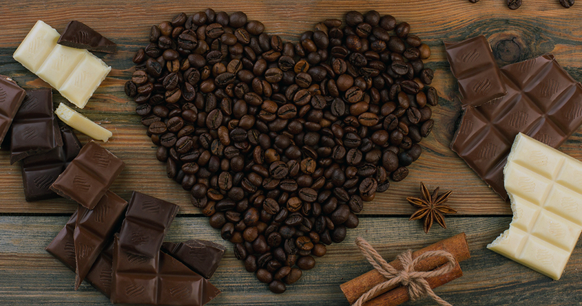 Et hjerte laget med kaffebønner ligger på et bord, med sjokolade rundt.