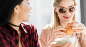To kvinner fra millenniumsgenerasjonen sitter på en kafé og drikker kaffe og spiser croissant.