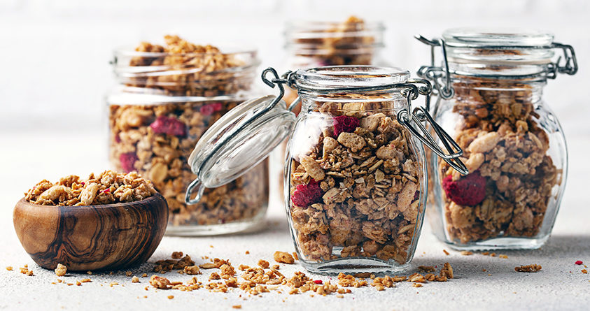 Fire glasskrukker fylt med hjemmelaget kaffegranola står på et bord.