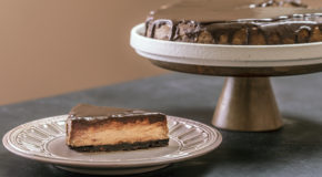 Et kakestykke av en kaffeostekake ligger på en tallerken, med resten av kaken stående i bakgrunnen.