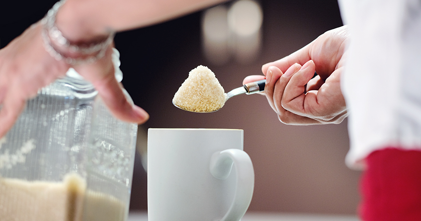 En kvinne putter en toppet teskje med sukker oppi en kaffekopp