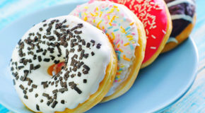 Et tallerken med fire fargerike donuts står på et bord.